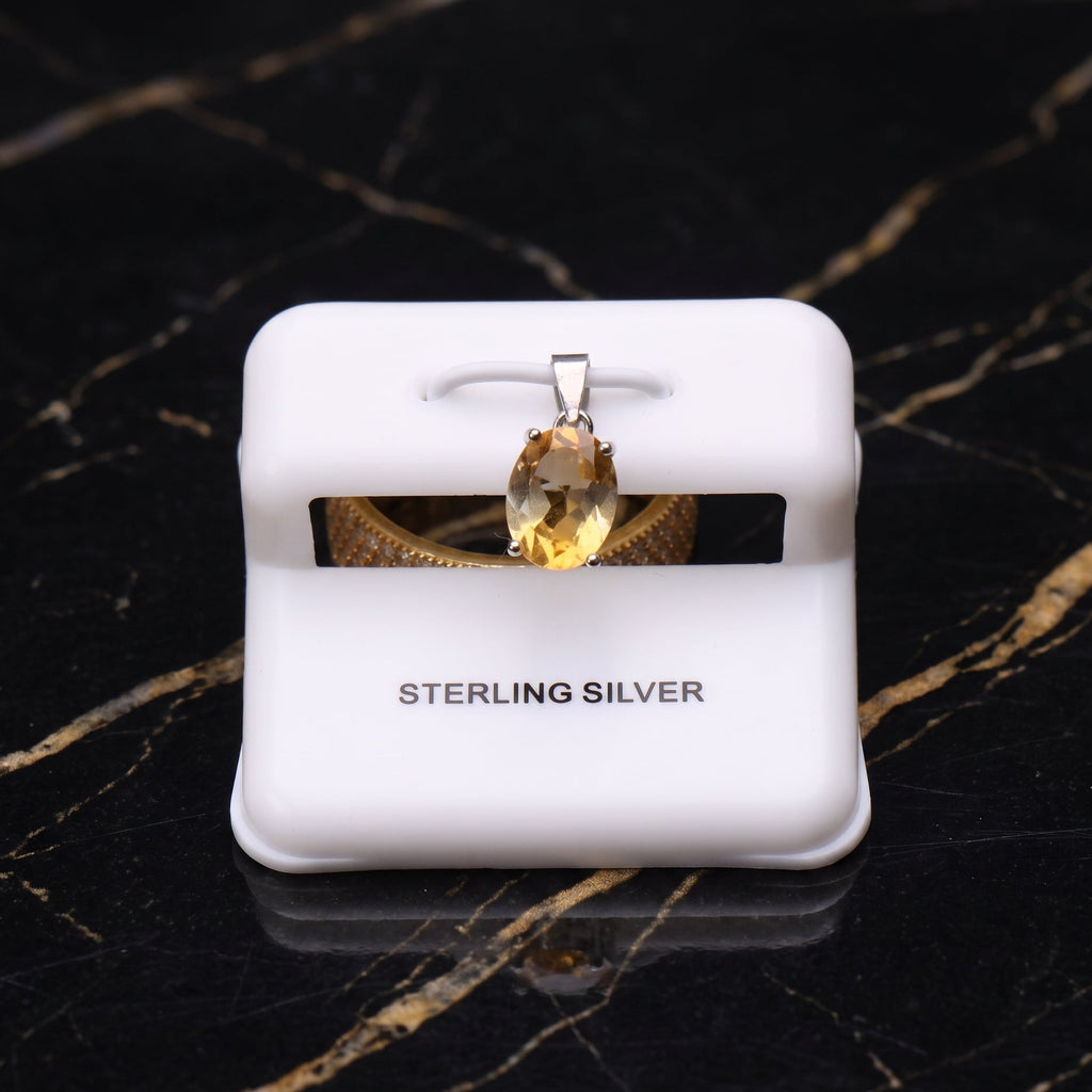 Sterling silver pendant with an oval-cut yellow gemstone, displayed on a white jewelry stand over a black marble background.