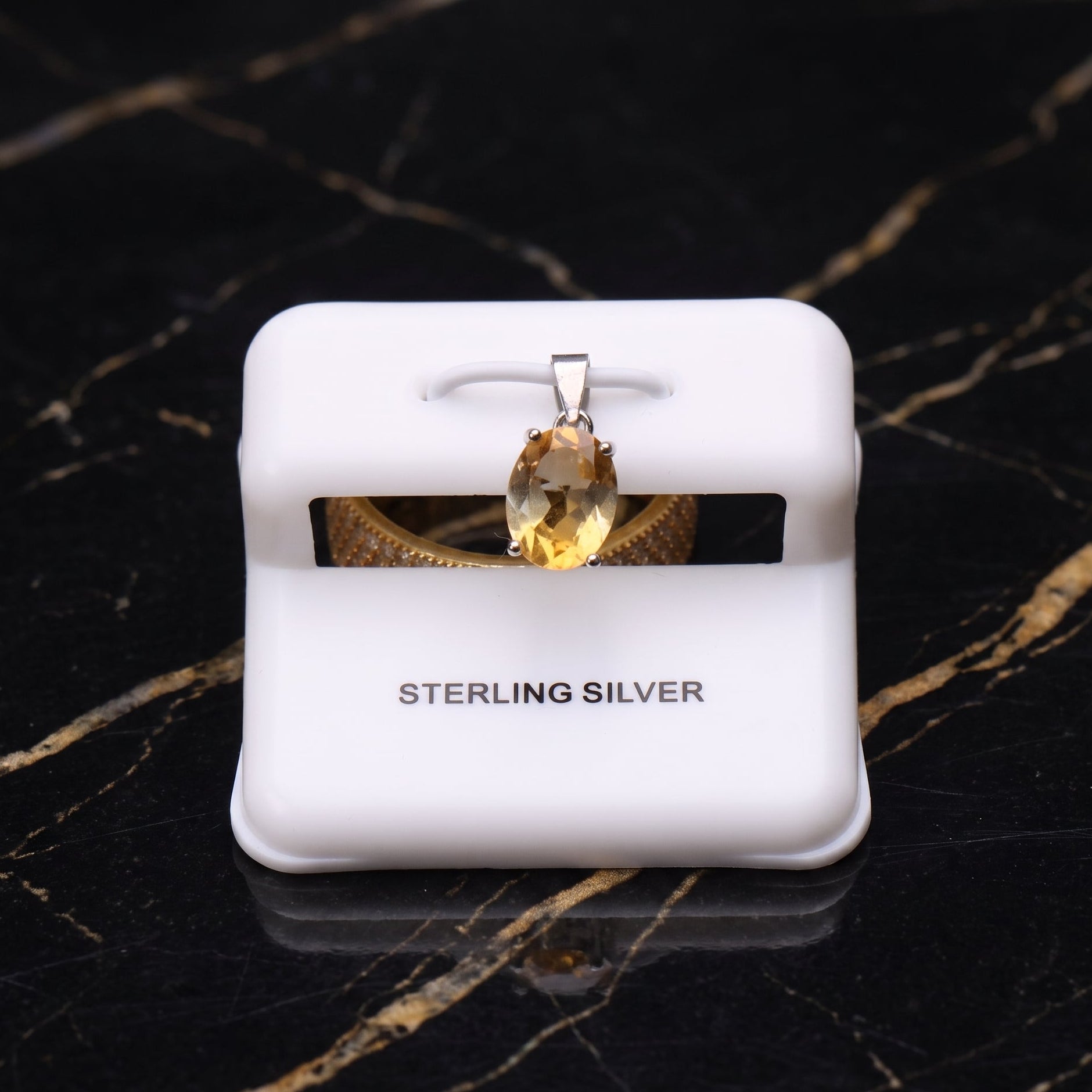 Sterling silver pendant with an oval-cut yellow gemstone, displayed on a white jewelry stand over a black marble background.
