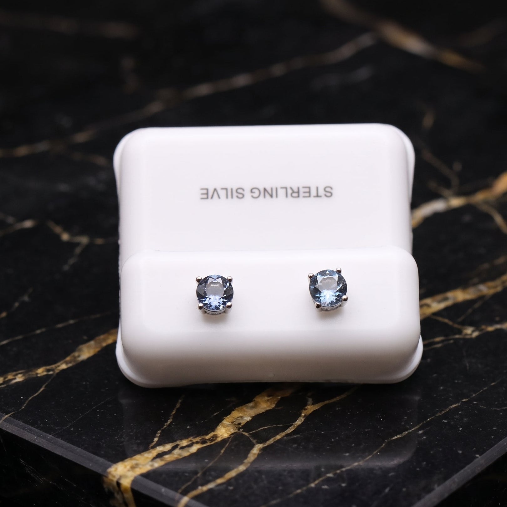 A pair of sterling silver stud earrings with clear round-cut gemstones, displayed on a white jewelry stand. The stand has 'STERLING SILVE' printed on it.