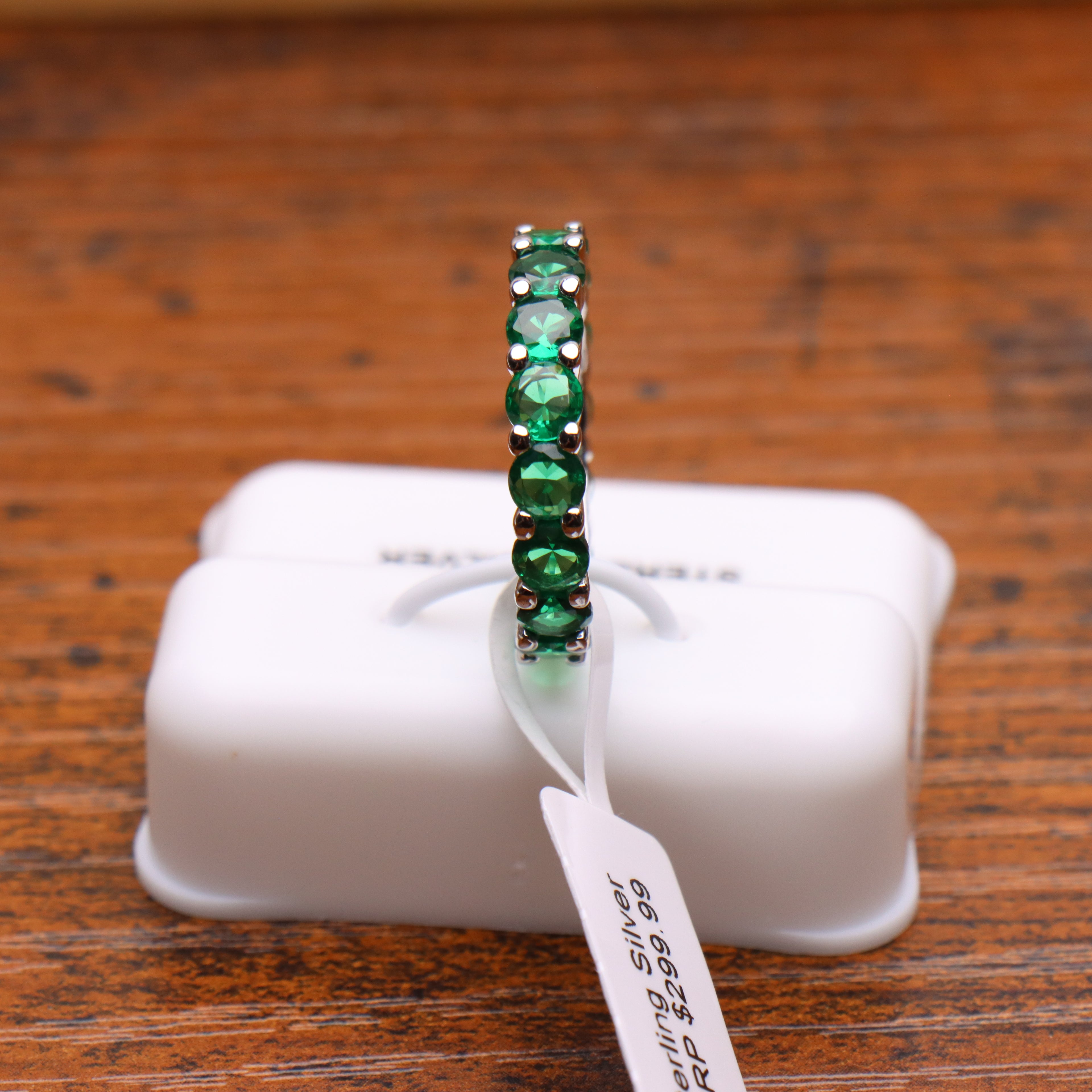 Green CZ eternity band ring in 925 sterling silver with round cut stones on a white display stand