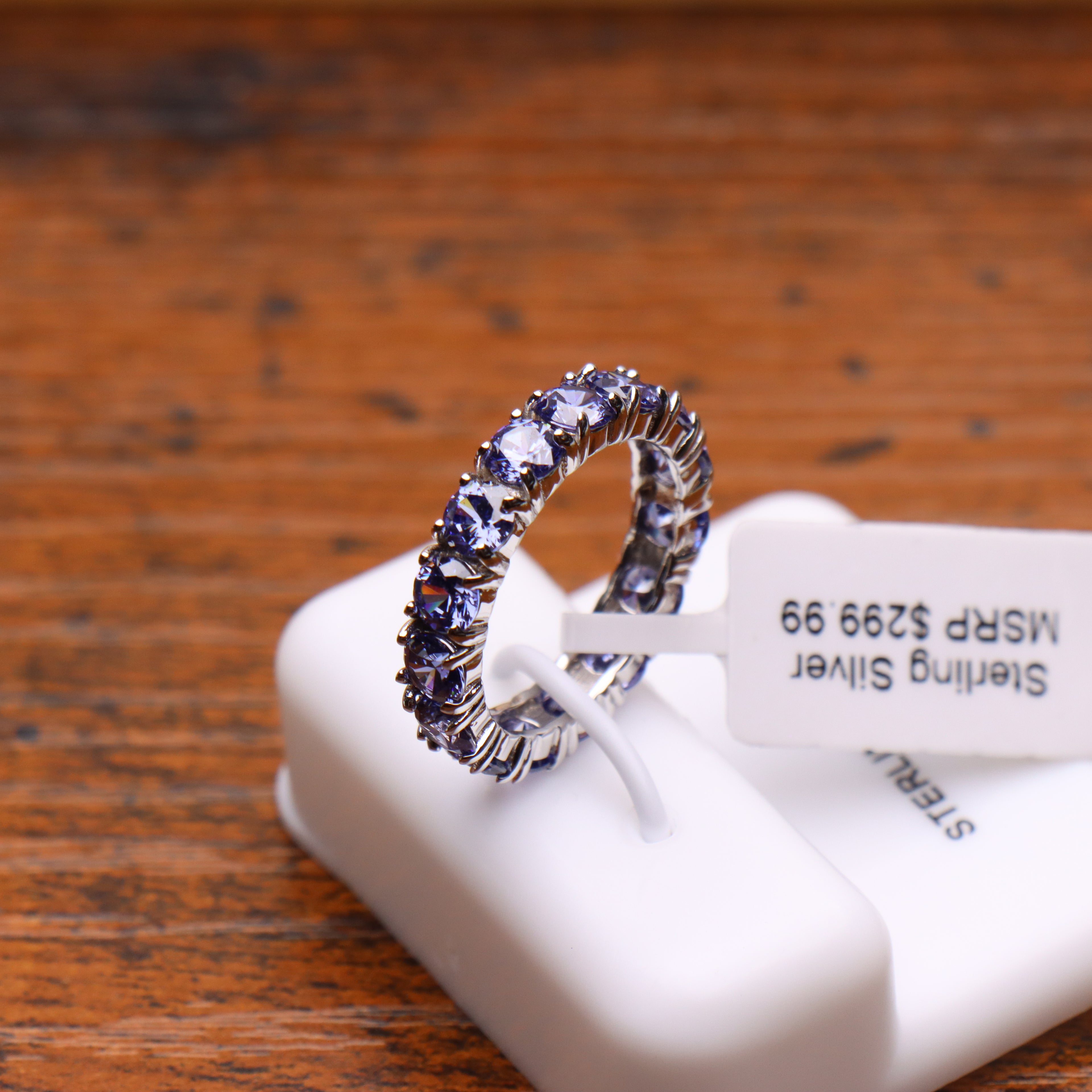 Tanzanite color round cut CZ eternity band in 925 sterling silver on a white display stand