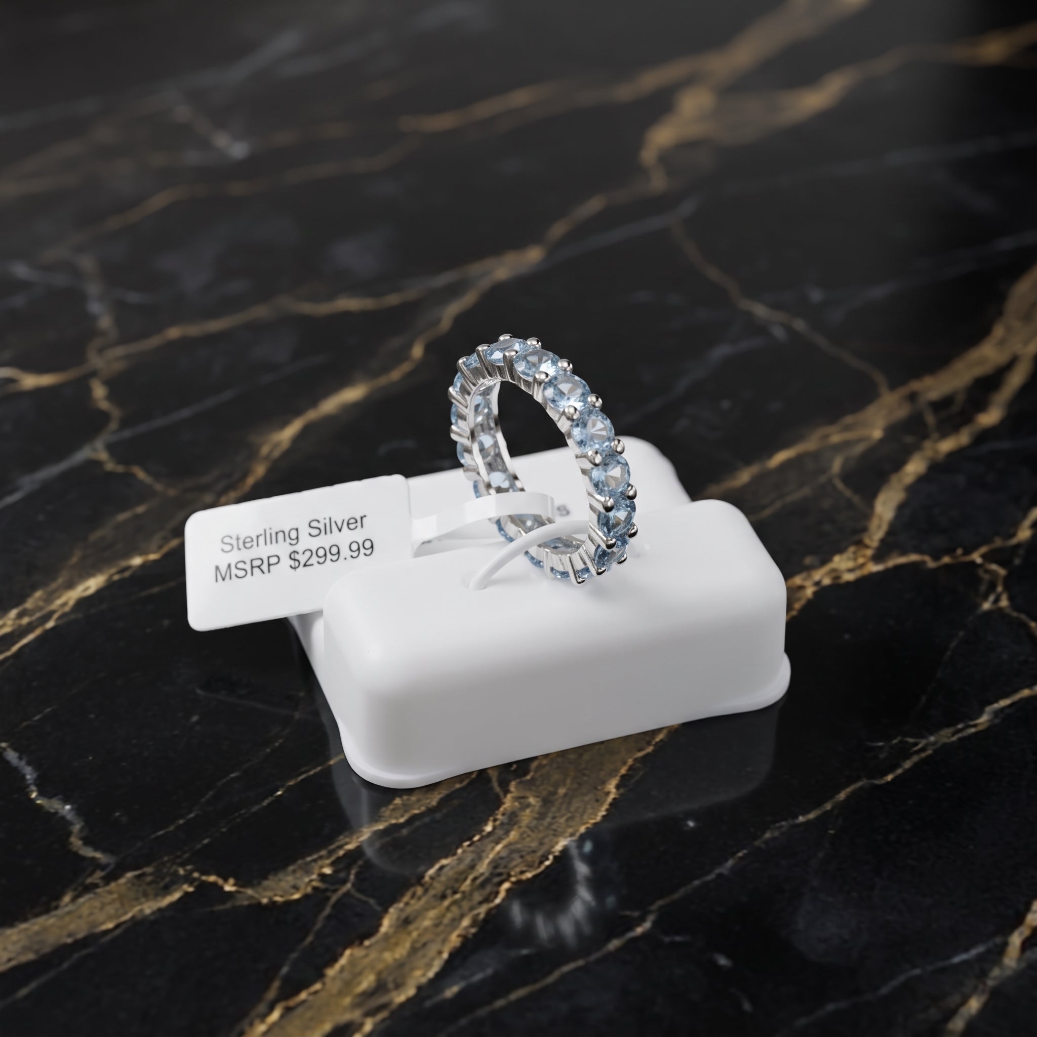 A sterling silver eternity band ring with clear stones, displayed on a white plastic stand with a price tag that reads 'Sterling Silver MSRP $299.99'.