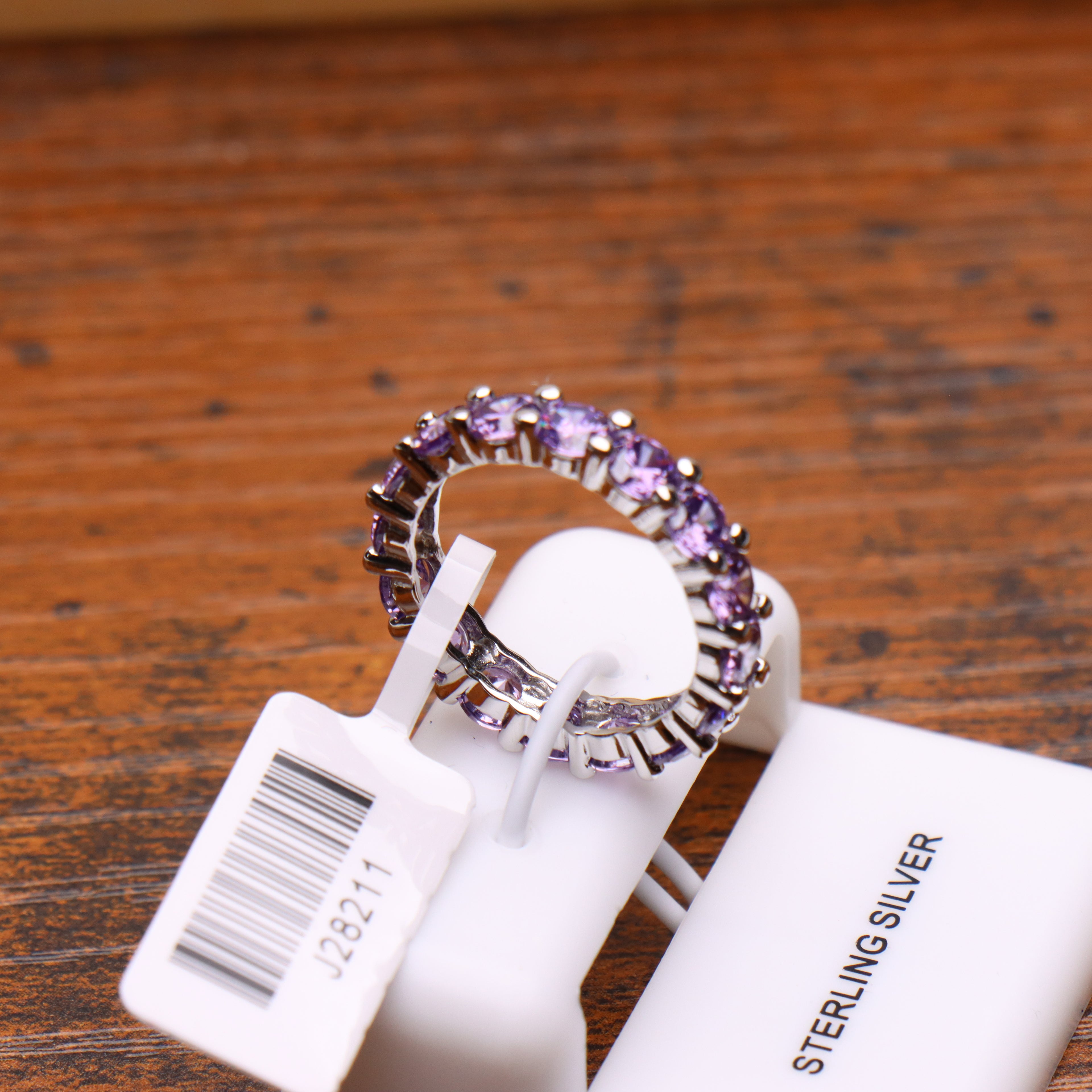 Purple CZ eternity band ring in 925 sterling silver with round cut stones on a display stand