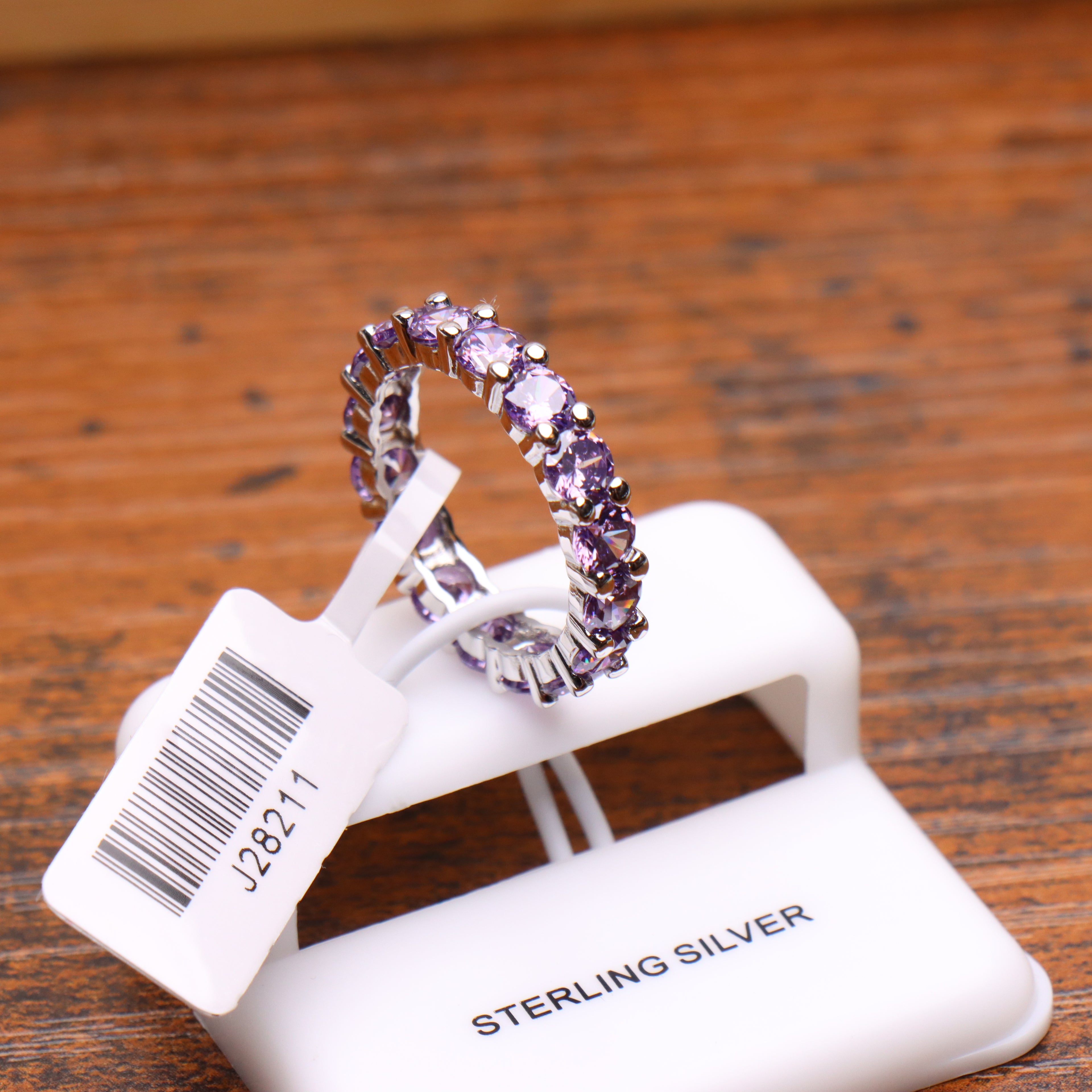 Purple CZ eternity band ring in 925 sterling silver with round cut stones on a white display stand