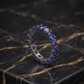 Dark blue round cut CZ eternity band ring in 925 sterling silver on a black marble surface