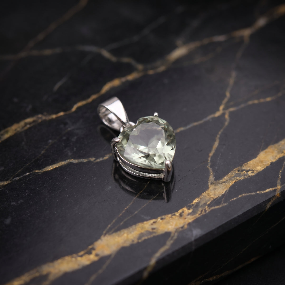 A heart-shaped clear gemstone pendant in a silver bezel setting, resting on a black and gold veined marble surface.