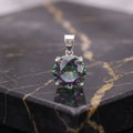 A round-cut iridescent gemstone pendant in a silver four-prong setting, displayed on a polished black marble slab with gold veining. mystic topaz