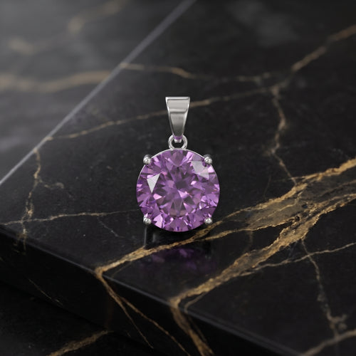 A round-cut purple gemstone pendant in a silver-toned setting, displayed on a black and gold veined marble surface. amethyst