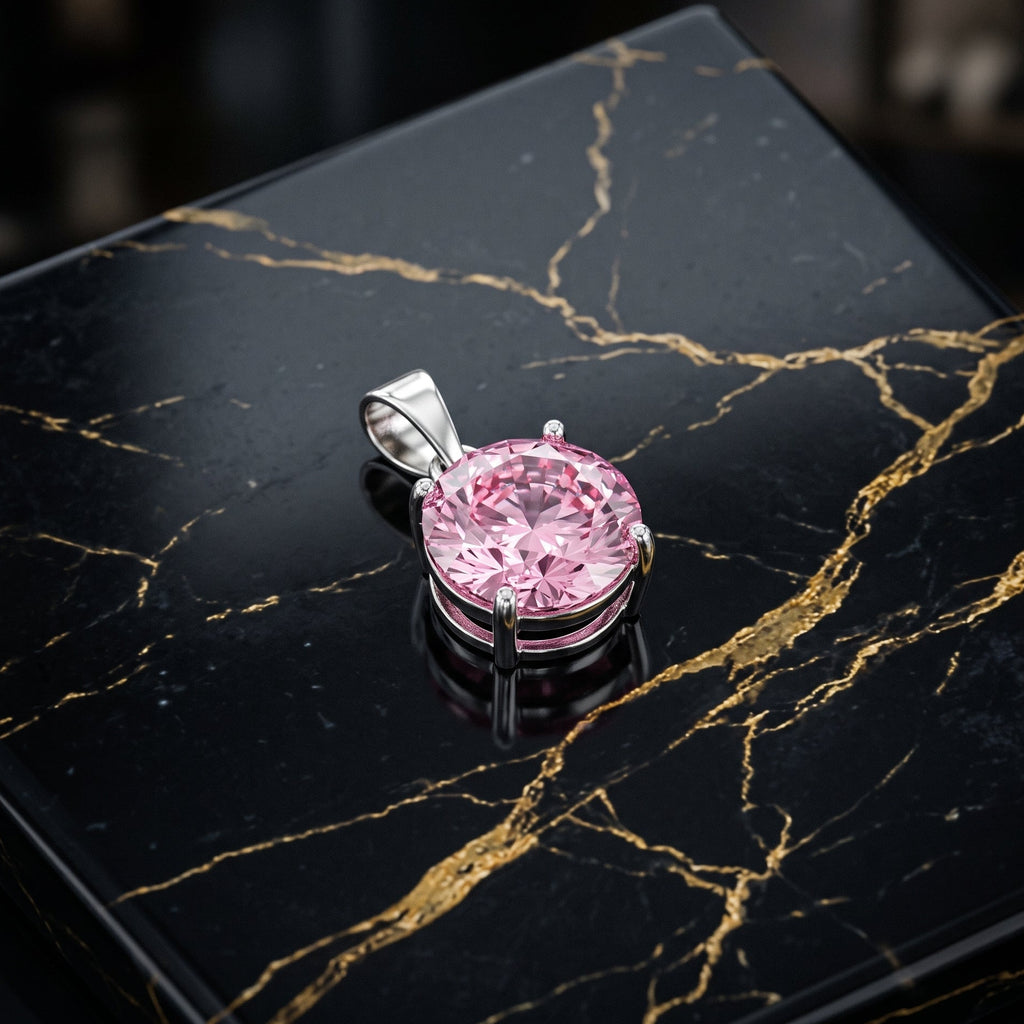 A round pink gemstone pendant in a silver-toned prong setting, displayed on a glossy black marble surface with gold veining.
