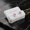 A pair of silver stud earrings with round pink gemstones, displayed on a white jewelry stand over a black marble surface with gold veining.