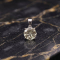 A round-cut pale yellow gemstone pendant set in a silver-toned metal prong, displayed on a black and gold veined marble surface.