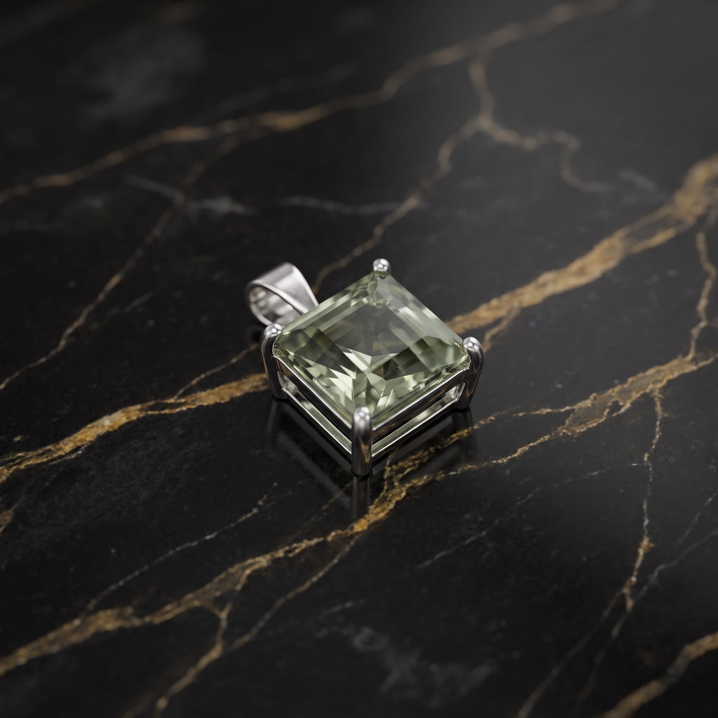 A square-cut green gemstone pendant in a silver-toned metal setting, displayed on a black marble surface with gold veining.