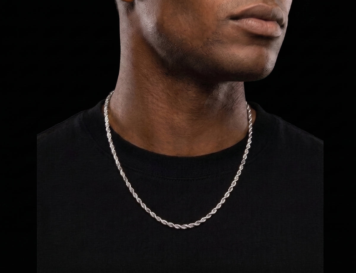 A close-up of a man wearing a silver-toned twisted rope chain necklace against a solid black background.