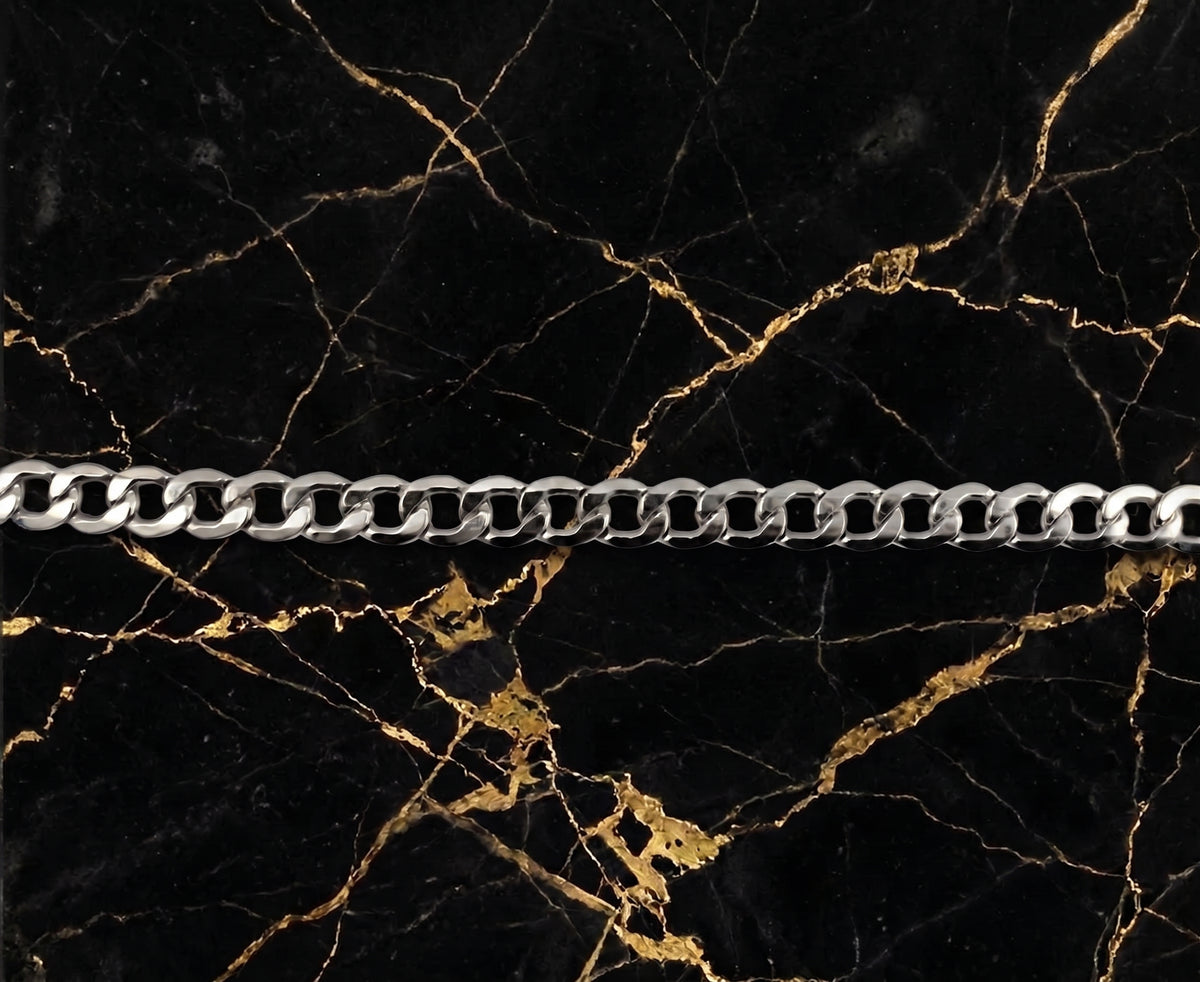 A silver-toned metal curb chain laid horizontally across a black marble surface with prominent gold veining.