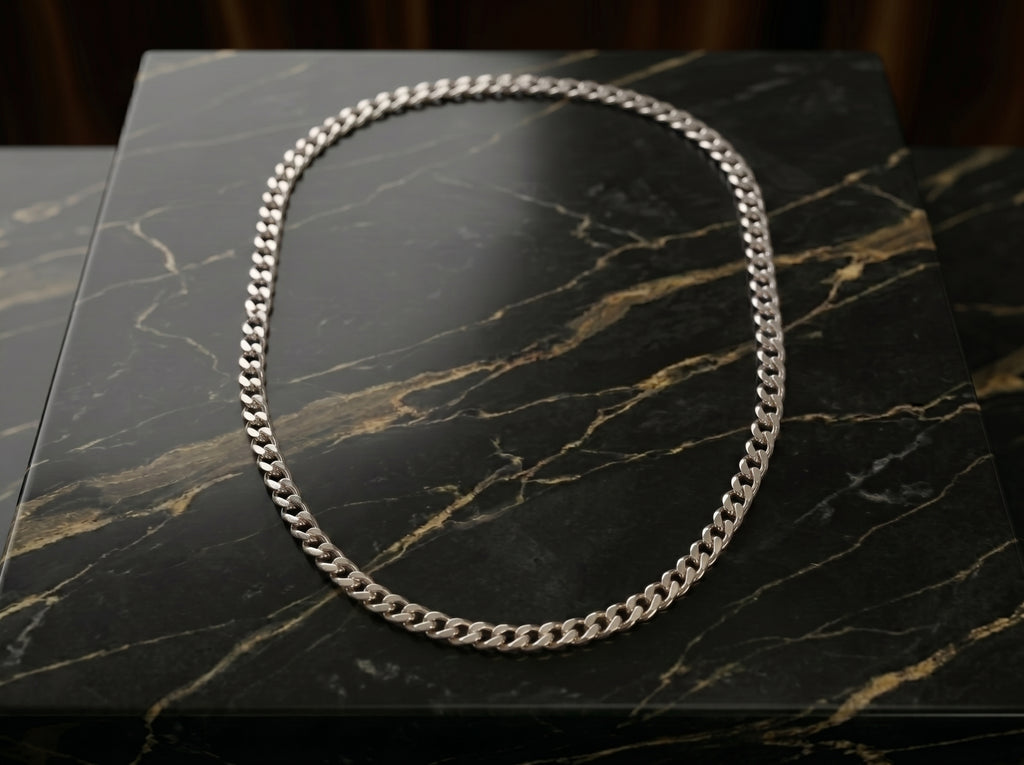 A silver-toned Cuban link chain necklace arranged in an oval shape on a black marble surface with gold veining.