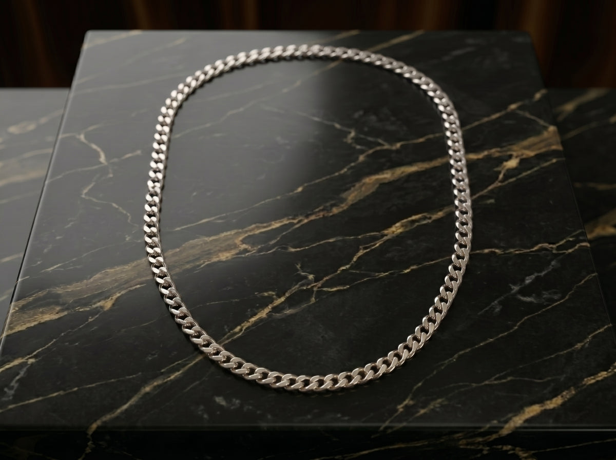 A silver-toned Cuban link chain necklace arranged in an oval shape on a black marble surface with gold veining.